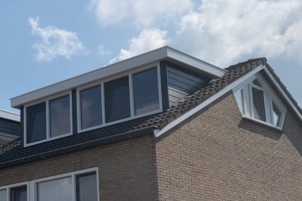 Dakkapel met grote ramen op een woning onder een heldere lucht.