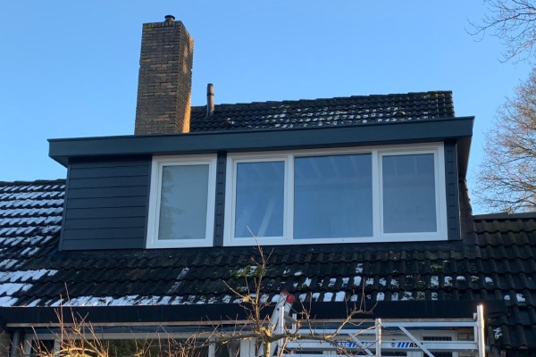 Dakkapel met grote ramen geplaatst op een woning met een schuin dak en schoorsteen, deels besneeuwd dak.